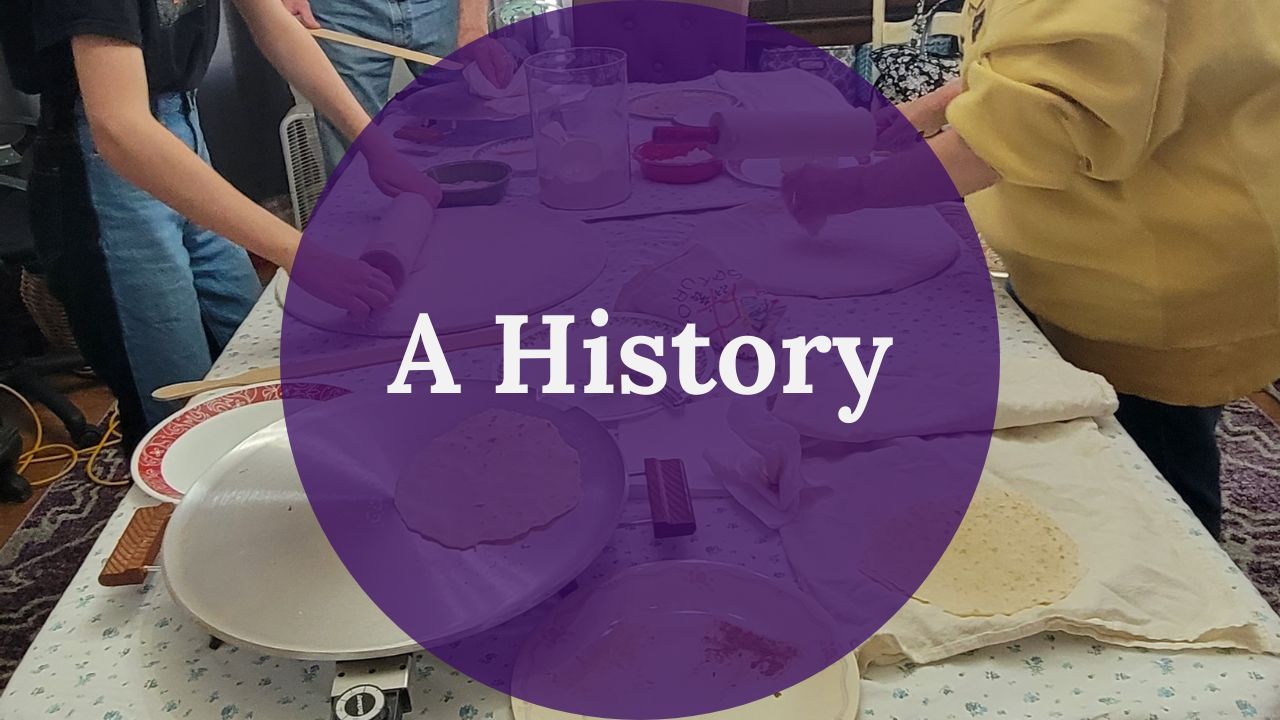 A purple circle reading A History in white text over a picture of lefse tools. These tools include griddles, spatulas, plates, rolling pins, and rolling stones. There are three sets of arms in the photo as the people prepare lefse.