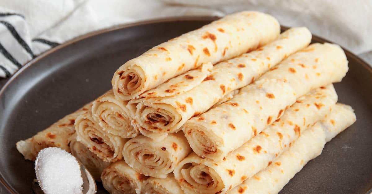 Plate of a rolled lefse stack and a spoonful of sugar on a dark plate.